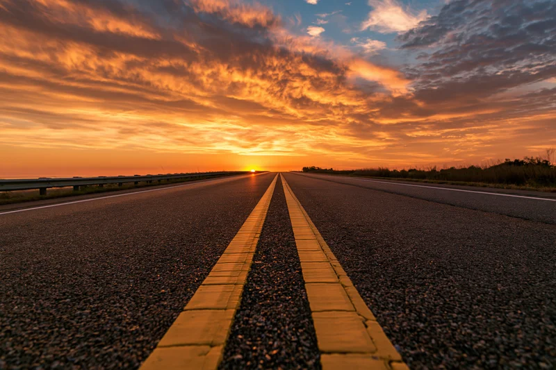 Empty two-lane asphalt highway stretching to the horizon at sunset