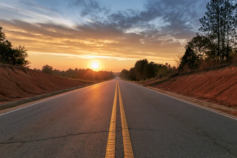 Empty two-lane asphalt highway stretching toward the horizon at sunset