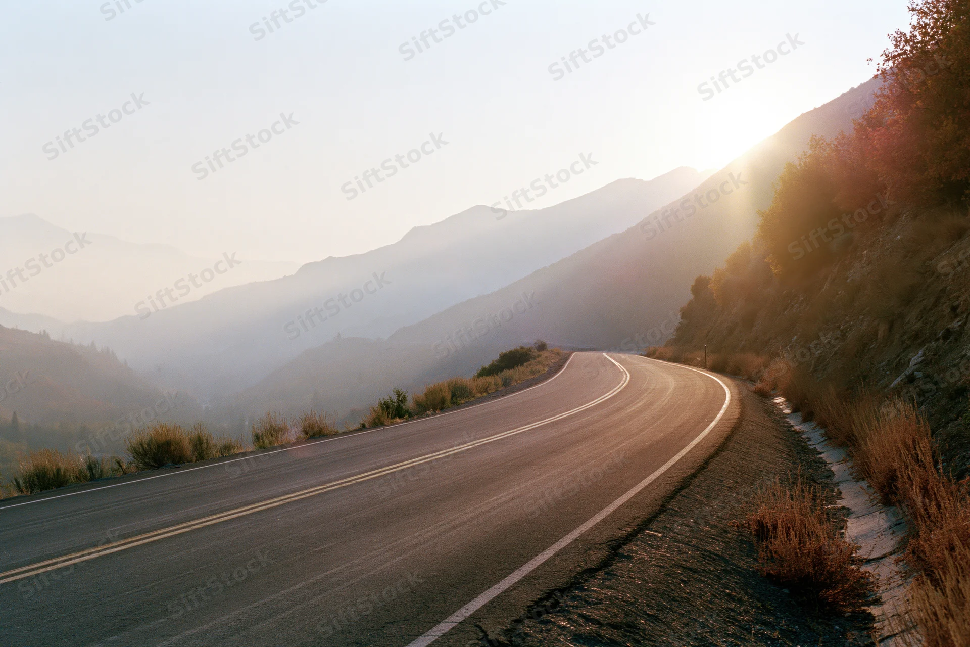 Winding asphalt road curving through misty mountains at sunrise