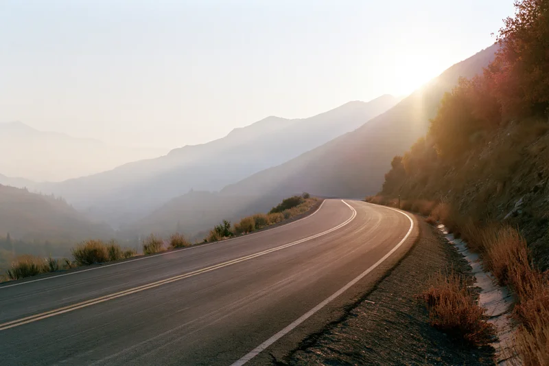 Winding asphalt road curving through misty mountains at sunrise