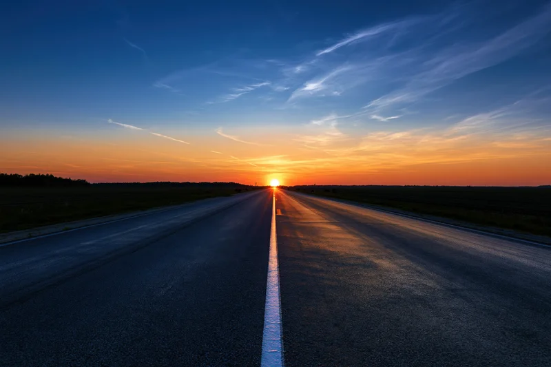 Straight asphalt road stretching to the horizon at sunset over rural fields