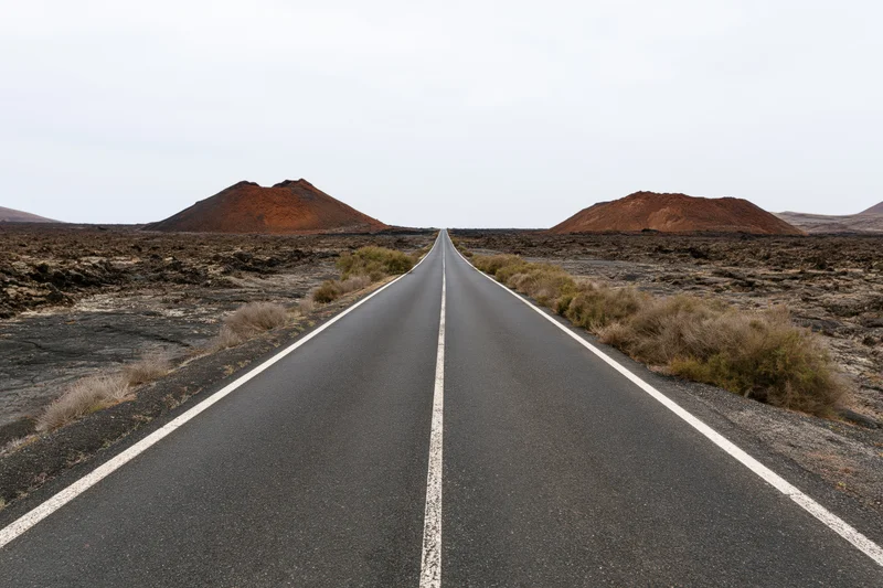 Straight asphalt road stretching through volcanic desert landscape toward horizon