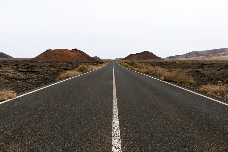 Straight asphalt road stretching to the horizon through volcanic desert landscape