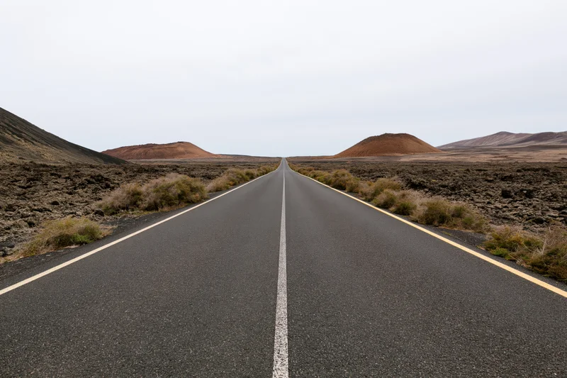 Straight asphalt road stretching to the horizon through a barren volcanic desert landscape