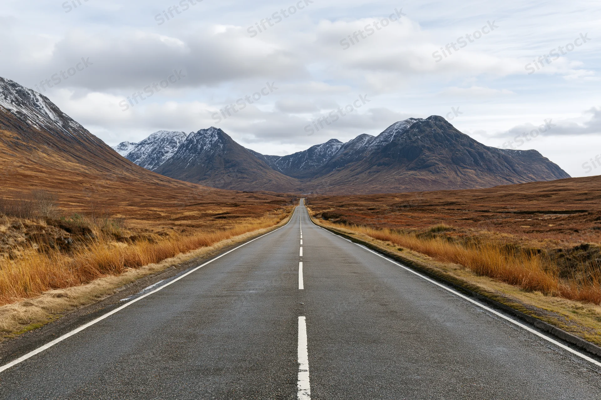 Straight asphalt road stretching through a mountain valley in the Scottish Highlands