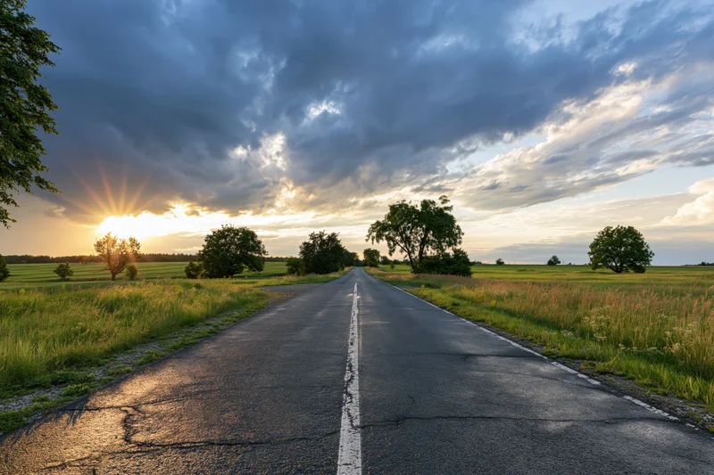 Empty asphalt road stretching toward the horizon through a rural landscape at sunset