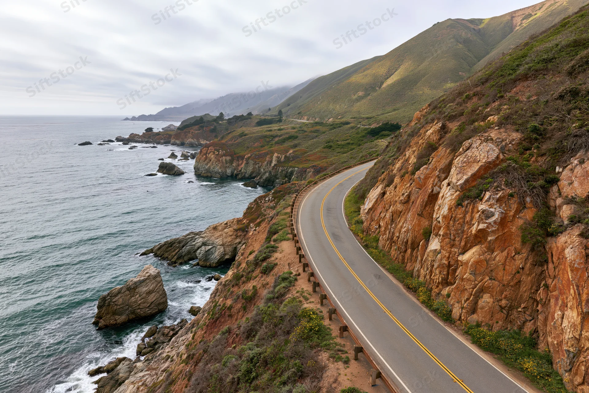 Winding two-lane highway along steep cliff overlooking ocean and mountains