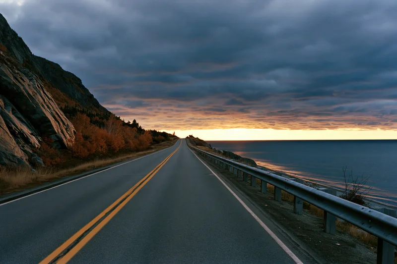 Two-lane highway stretching toward the horizon along a rocky coastline at sunset