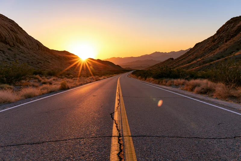 Empty two-lane highway curving through desert landscape at sunset