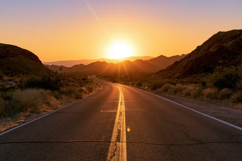 Winding asphalt highway through desert landscape at sunset with mountains on horizon