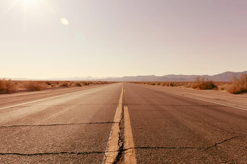 Straight asphalt highway stretching into the desert landscape with distant mountains under a bright sun