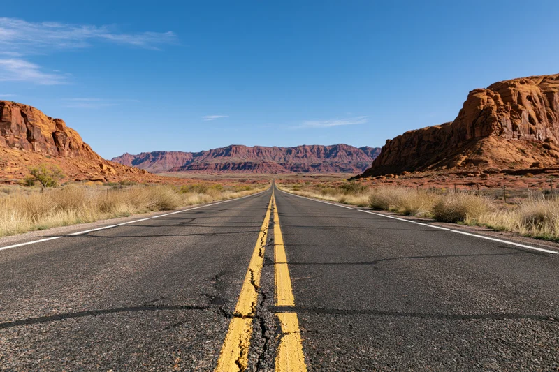 Straight asphalt highway stretching toward distant red rock mesas in desert landscape