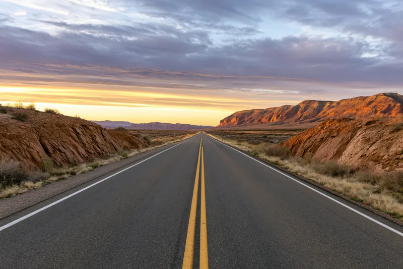 Straight two-lane highway through desert landscape at sunset