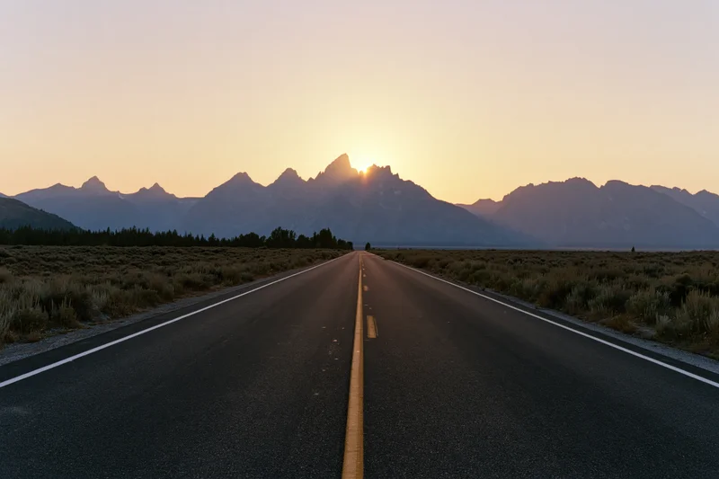 Straight asphalt highway stretching toward jagged mountain peak at sunset