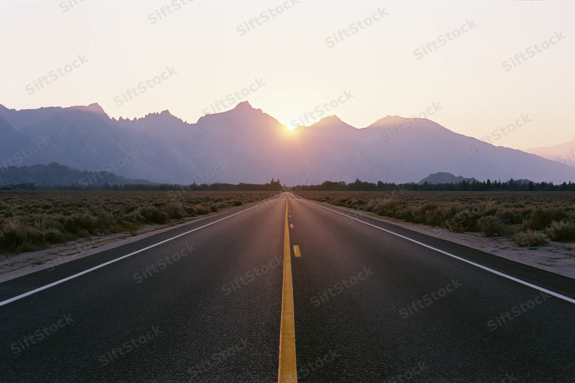 Straight asphalt highway stretching toward jagged mountain peak at sunset