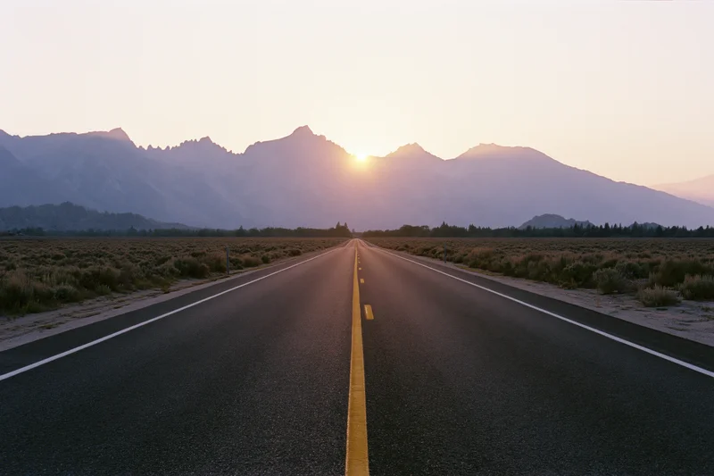 Straight asphalt highway stretching toward jagged mountain peak at sunset