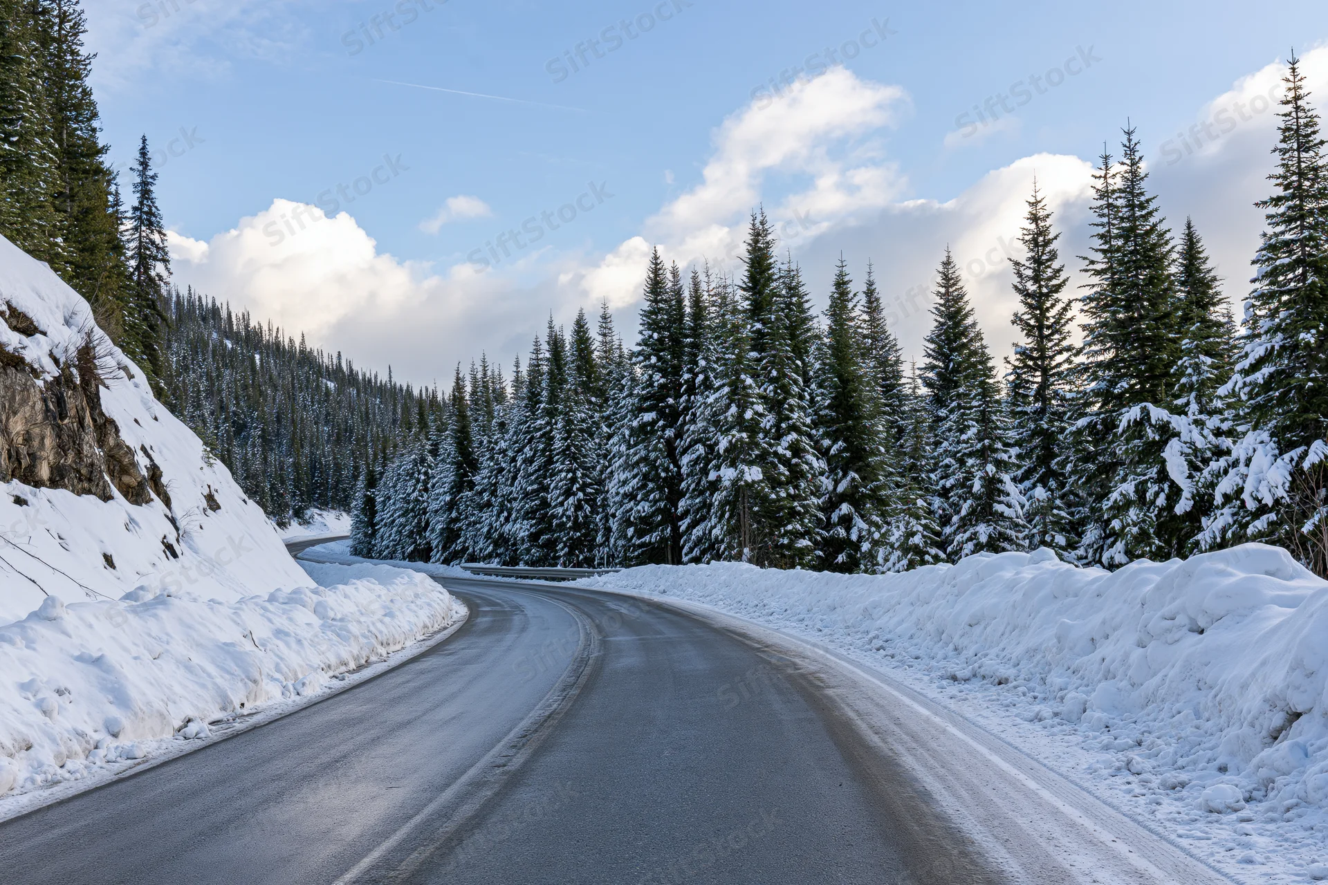 Winding asphalt road curves through snow-covered pine forest in mountain landscape