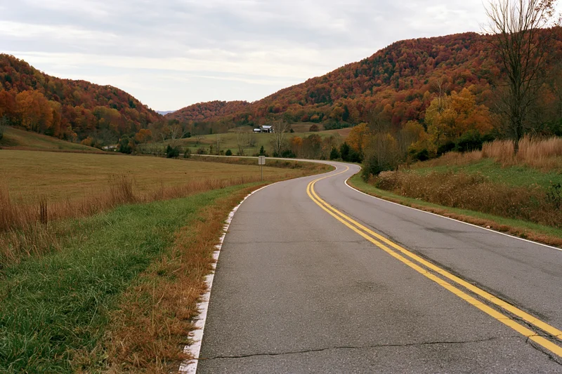 Winding rural highway with double yellow center line through autumn forested hills and fields