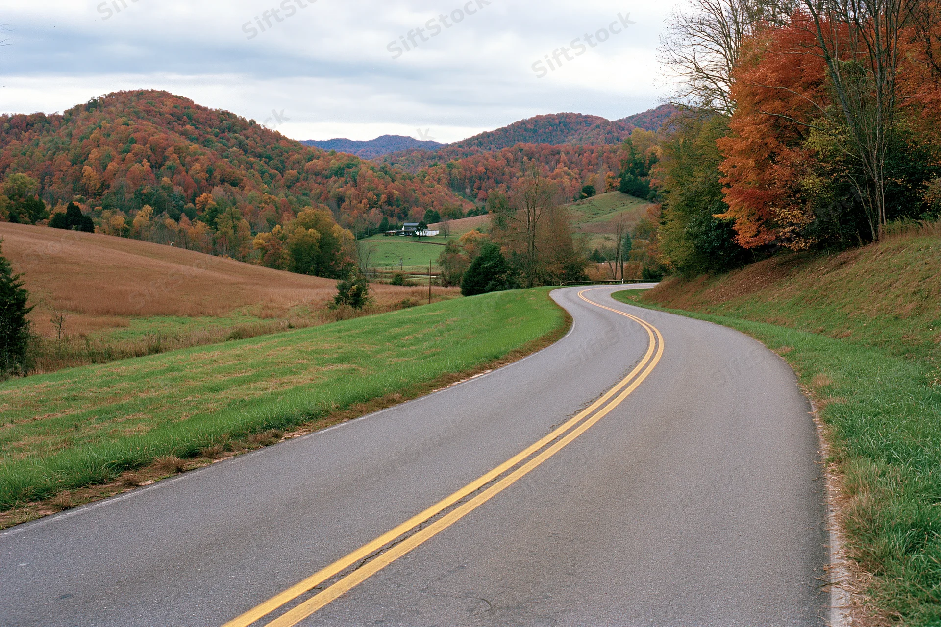 Winding two-lane asphalt road through autumn countryside with colorful trees and rolling hills