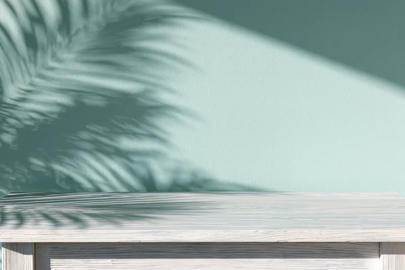 White-washed wooden tabletop with palm shadow against a mint green wall, copyspace for product display
