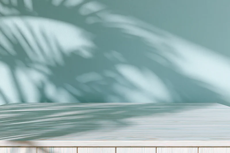 White-washed wooden tabletop with palm leaf shadows against a soft teal wall