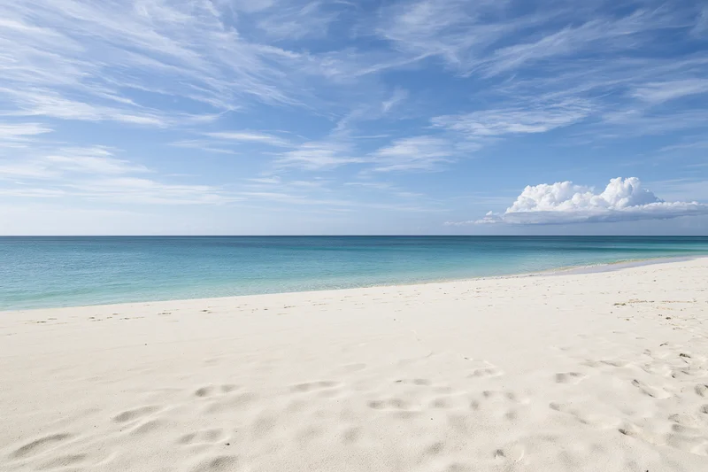 White sand beach stretching to calm turquoise ocean under blue sky with scattered clouds