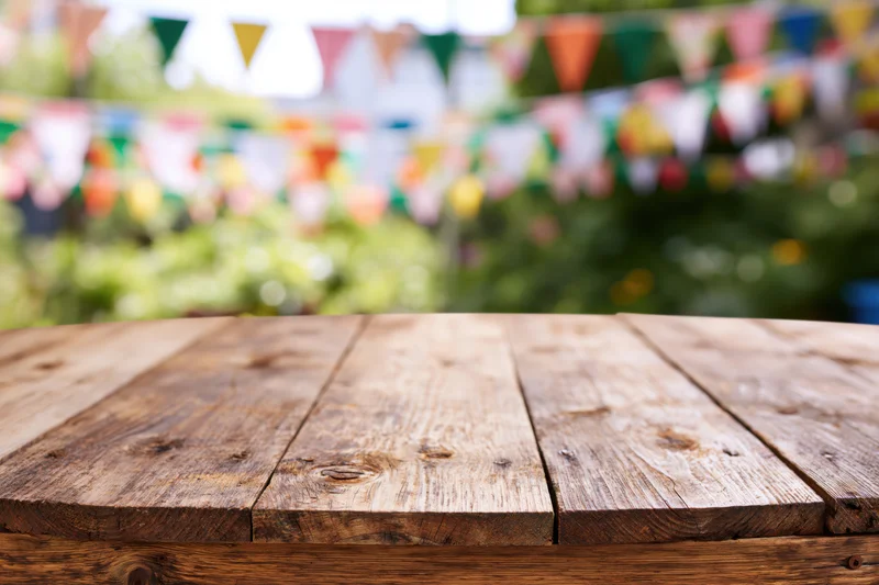Wooden table top in sharp focus with colorful bunting and greenery blurred in background
