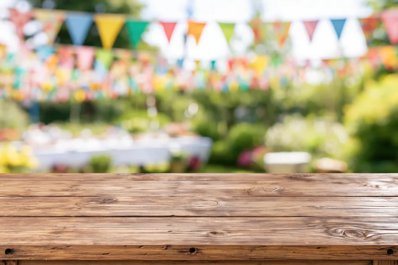 Wooden table surface in sharp focus with colorful bunting and greenery blurred in background