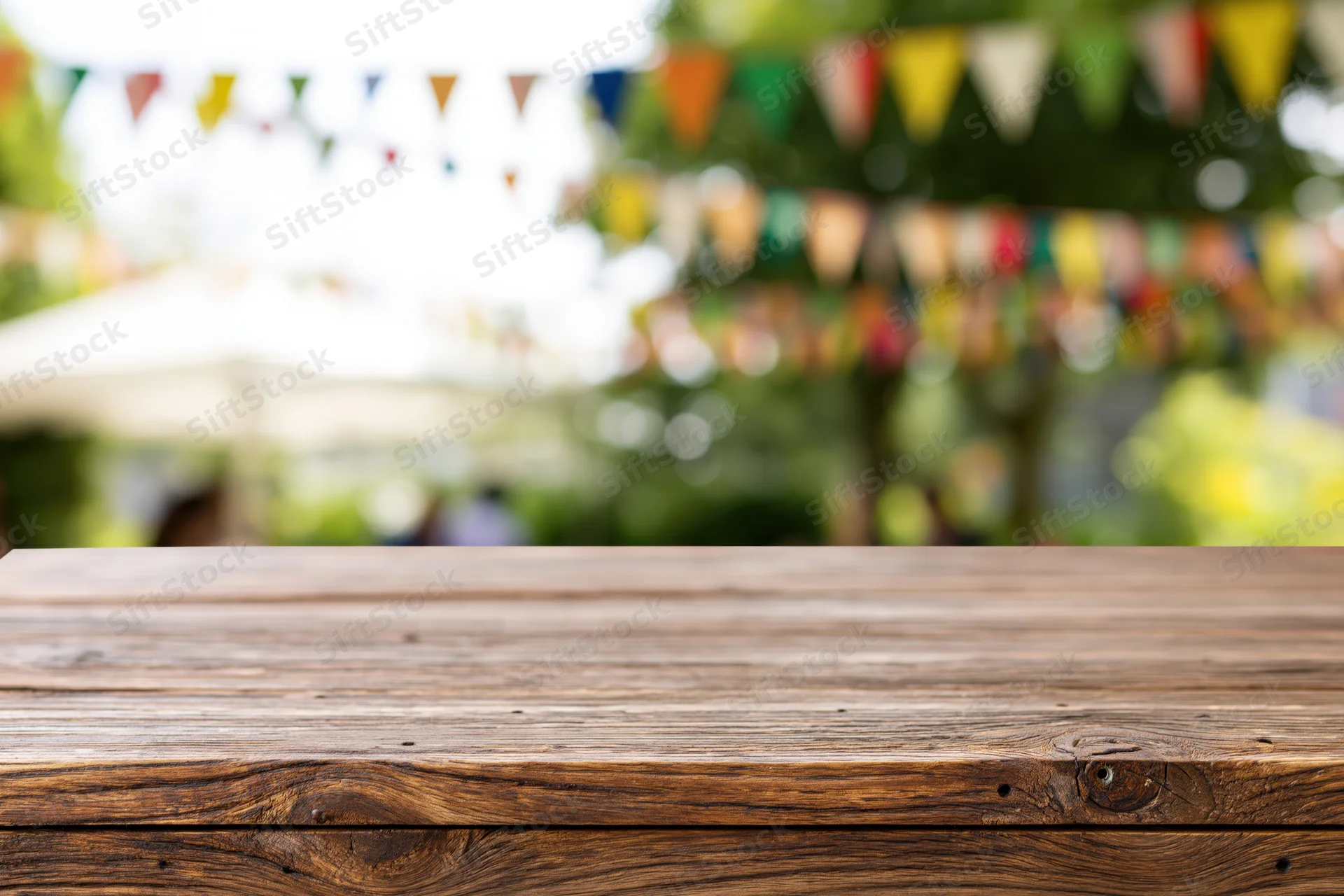 Empty wooden table in sharp focus with colorful bunting and greenery in blurred background outdoors