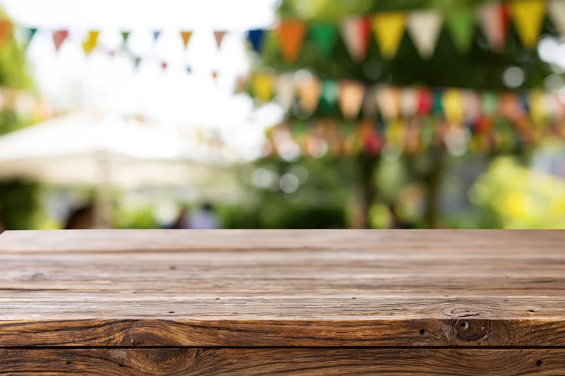 Empty wooden table in sharp focus with colorful bunting and greenery in blurred background outdoors