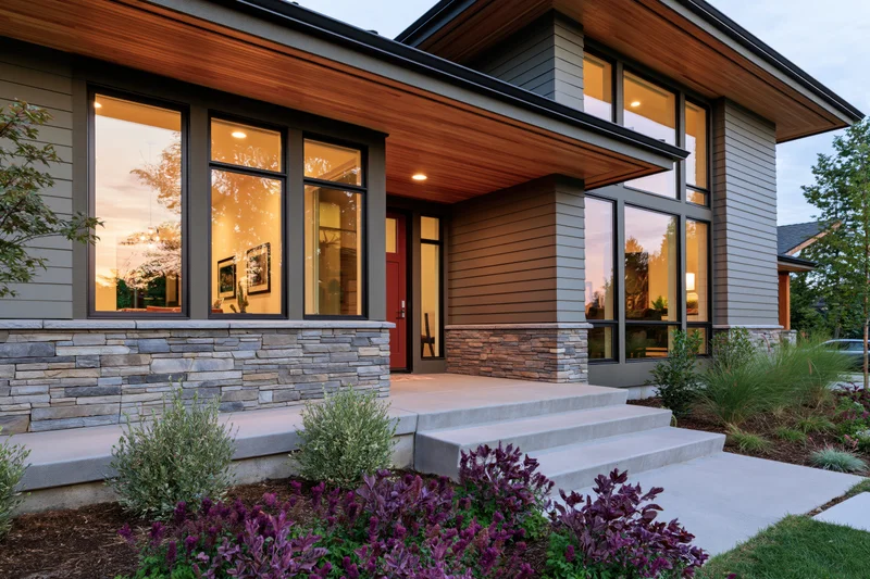 Modern craftsman home front entry with red door and stone facade at dusk