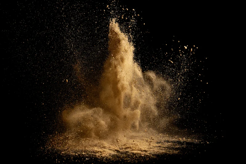 Golden-brown sand exploding upward in mid-air against black background
