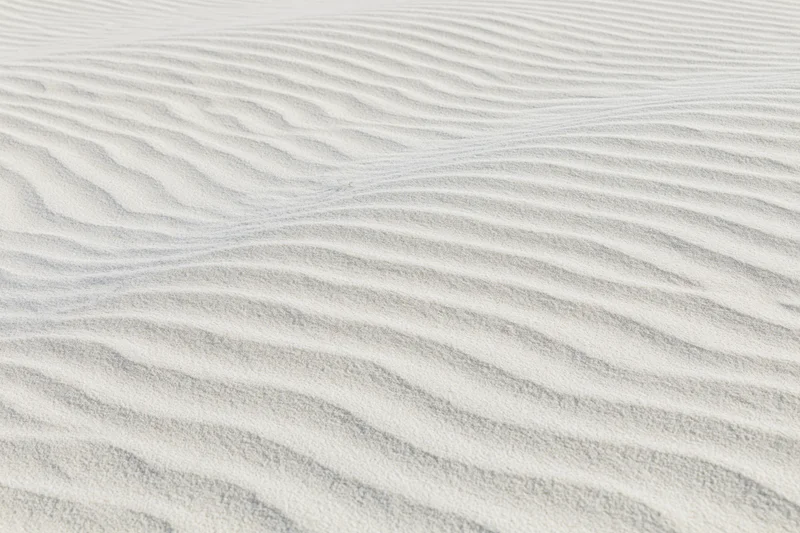 Wind-rippled white sand surface with gentle wave patterns across the frame