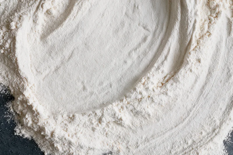 White wheat flour spread in a circular pattern on a dark surface, overhead flat lay view