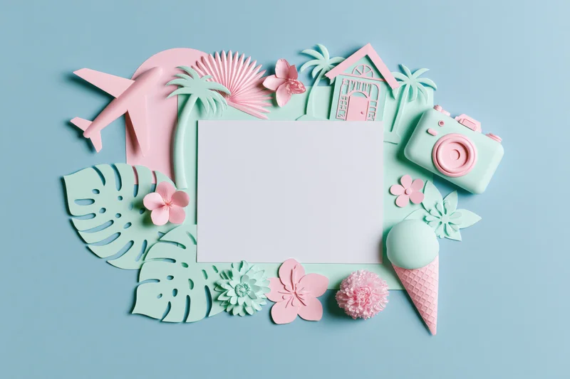 Flat lay arrangement of pastel paper cutouts including airplane, camera, ice cream, flowers and palm leaves around a blank card on a light blue background