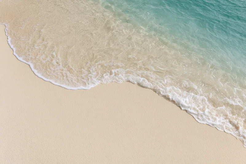 Gentle ocean wave washing onto clean sandy beach from above
