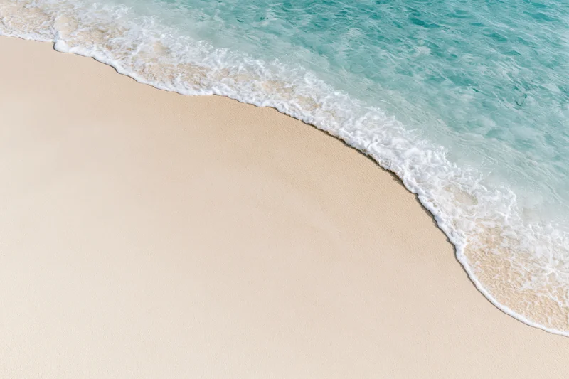 Gentle ocean wave washing onto a clean sandy beach from above