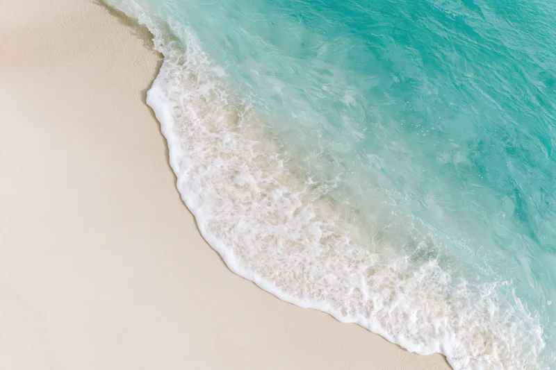 Gentle ocean wave washing onto clean white sand