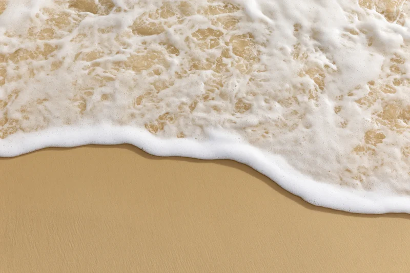 Gentle ocean wave washing over smooth wet sand at the shoreline