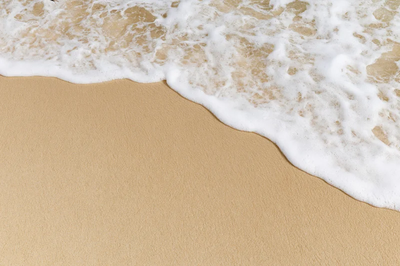 Gentle ocean wave washing over smooth wet sand at the shoreline