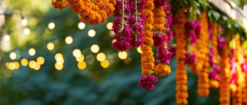 Marigold and pink flower garlands hanging outdoors with string lights in the background
