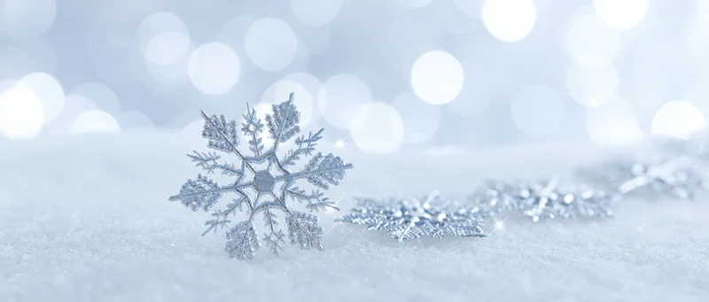 Decorative crystal snowflakes resting on soft snow with bokeh lights in background