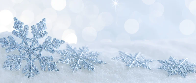 Decorative crystal snowflakes resting on soft snow with bokeh lights in background