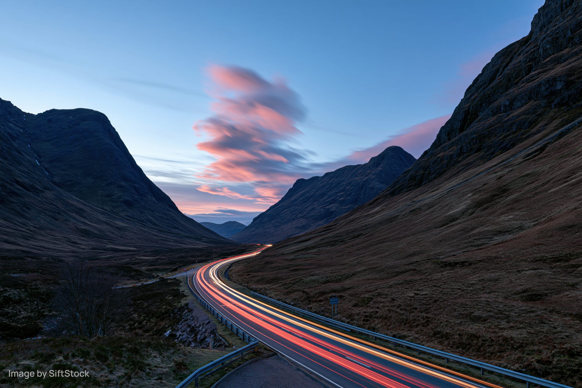 Light trails from vehicles moving along a winding mountain road in a valley at twilight