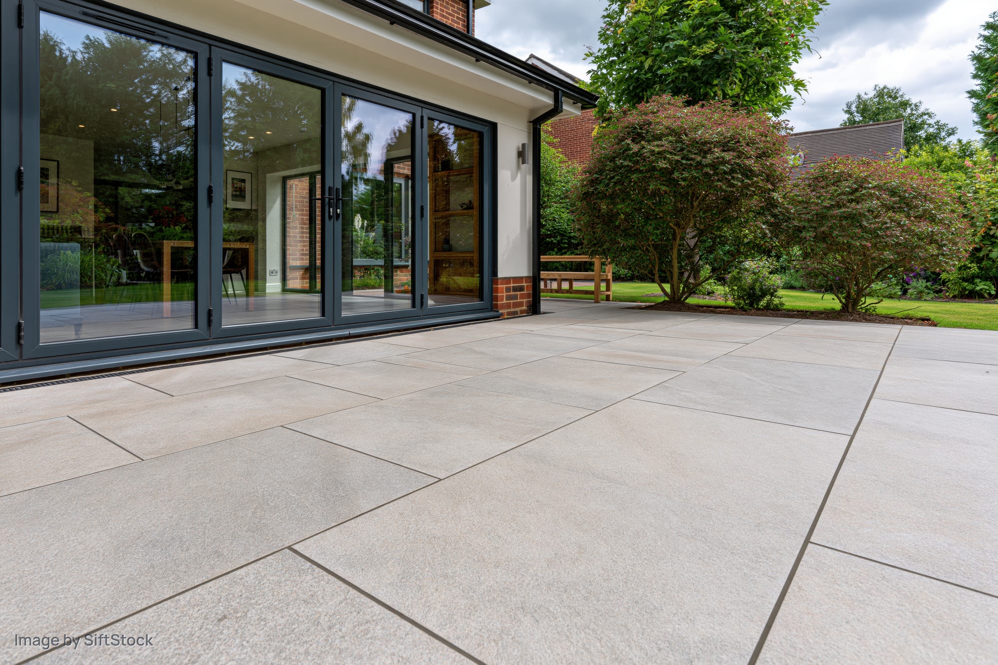 Large-format stone patio extending from modern house with bi-fold glass doors to garden area