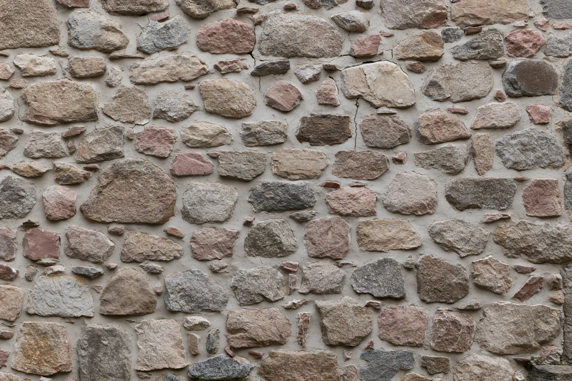 Close-up of an old rubble stone wall with irregularly shaped stones and mortar joints filling the frame