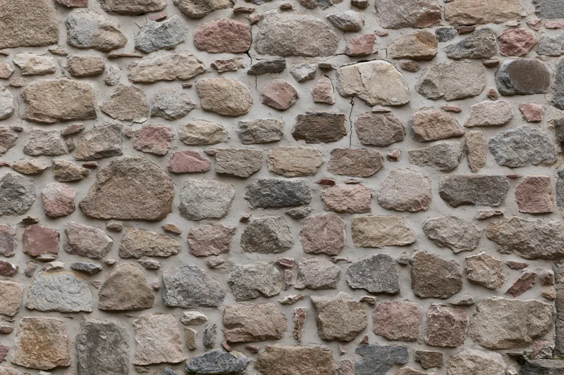 Close-up of an old rubble stone wall with irregularly shaped stones and mortar joints filling the frame