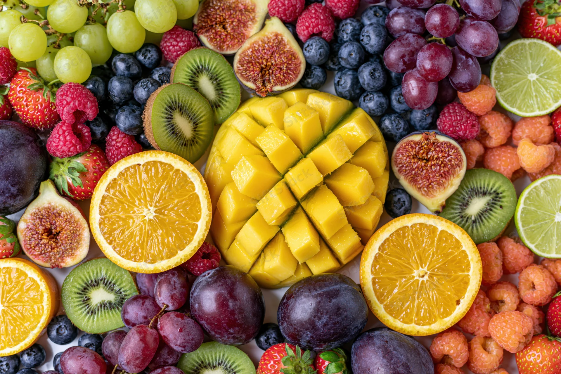 Overhead flat lay of assorted fresh cut and whole fruits arranged densely on white surface