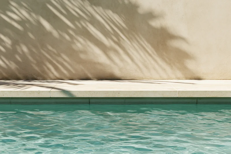 Calm turquoise pool water with palm leaf shadows on a smooth beige concrete wall