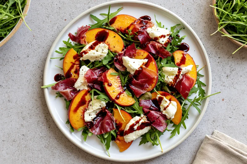 Peach and prosciutto salad with arugula and mozzarella on a white plate viewed from above